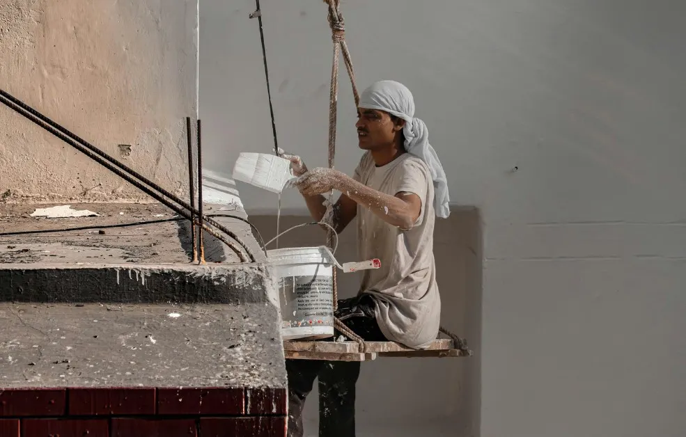 Operario en andamio colgante enfoscando la fachada de un edificio en Trobajo del Camino