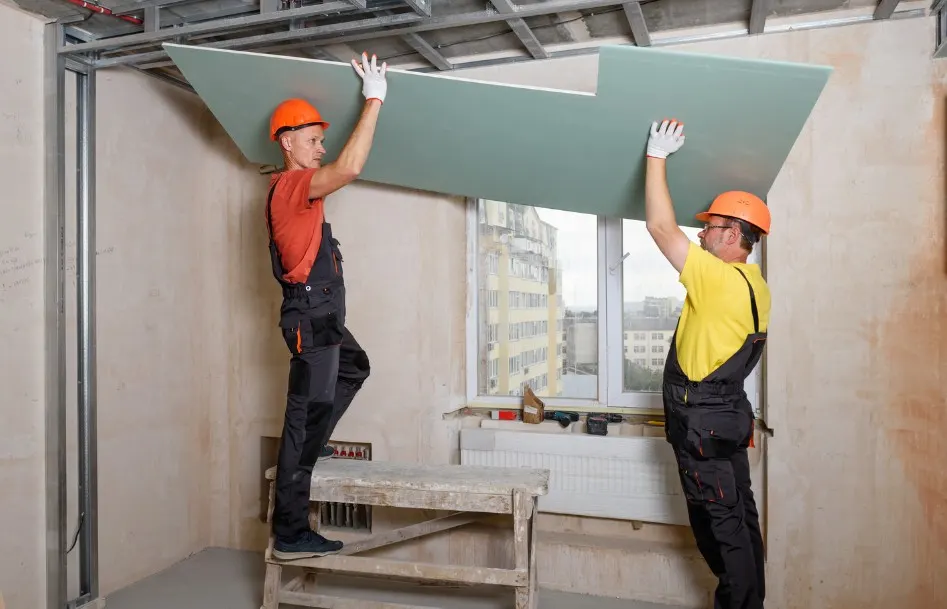 Dos operarios colocando una placa de pladur en el techo de una vivienda