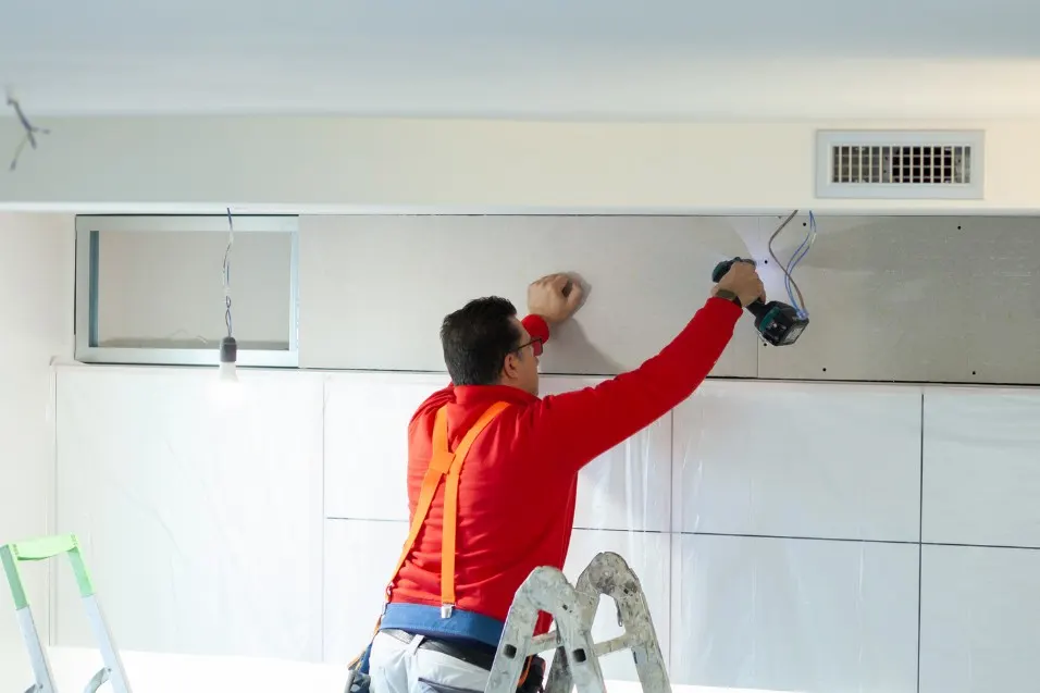 Operario atornillando placas de yeso laminado sobre una pared con atornillador