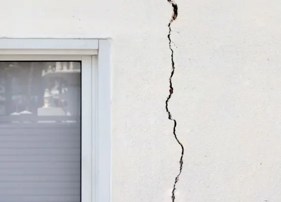 Grieta vertical fina de asentamiento en una fachada enfoscada y pintada de blanco, edificio urbano