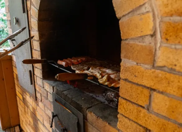 Barbacoa de ladrillo en uso con carne asándose sobre la parrilla metálica, porche exterior en Villaquilambre