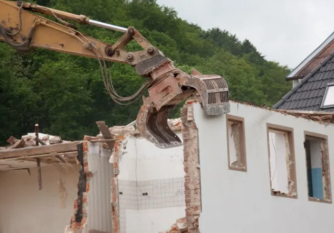 Excavadora con pinza hidráulica derribando el muro de fachada de una vivienda en La Bañeza