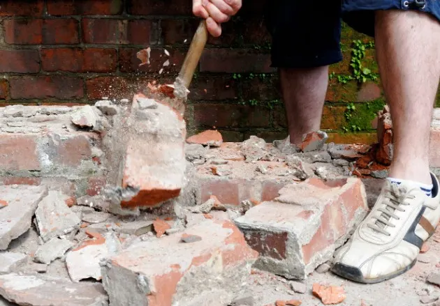 Trabajador demoliendo a mano un muro de ladrillo macizo con maza, León Centro