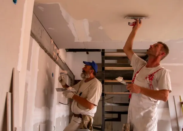 Dos operarios enluciendo un techo y pared de pladur con llana