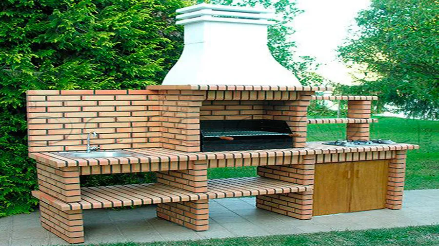 Barbacoa de ladrillo con campana blanca, fregadero y bancada en un jardín
