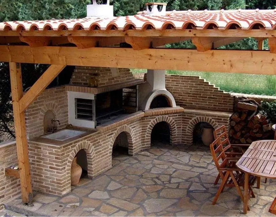 Barbacoa y horno de ladrillo bajo una pérgola de madera con tejado
