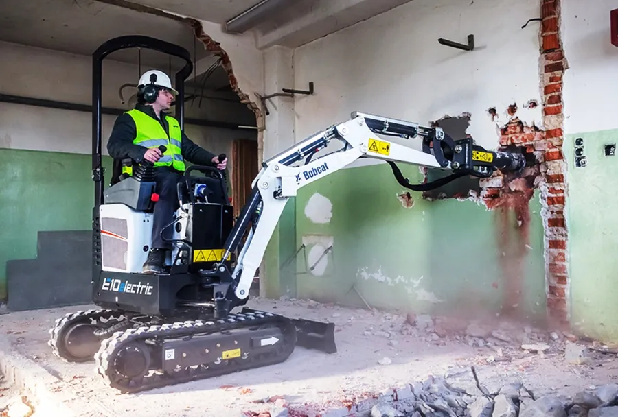 Miniexcavadora demoliendo un muro interior de un local