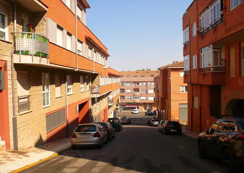 Calle residencial de Navatejera con bloques de pisos de ladrillo caravista y coches aparcados